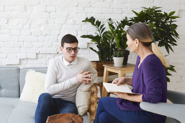 Candid shot of young man in glasses talking about his problems during psychological therapy session