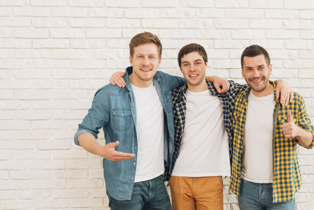 Group of three male friends standing together against white wall