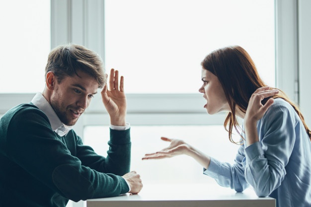 man and a woman are sitting at a table talking, quarreling with each other