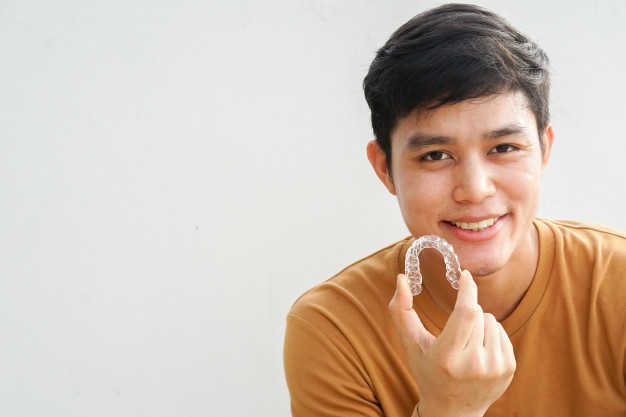 Man smiling with hand holding dental aligner retainer