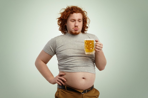 overweight fat young european man with curly red hair holding glass of beer