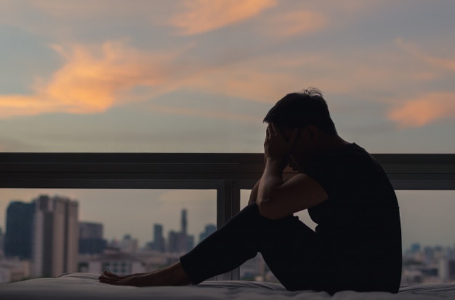 A person sitting and feeling depressed on bed with city view in dusk moment