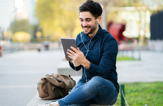 man having a video call on digital tablet while sitting on bench outdoors.