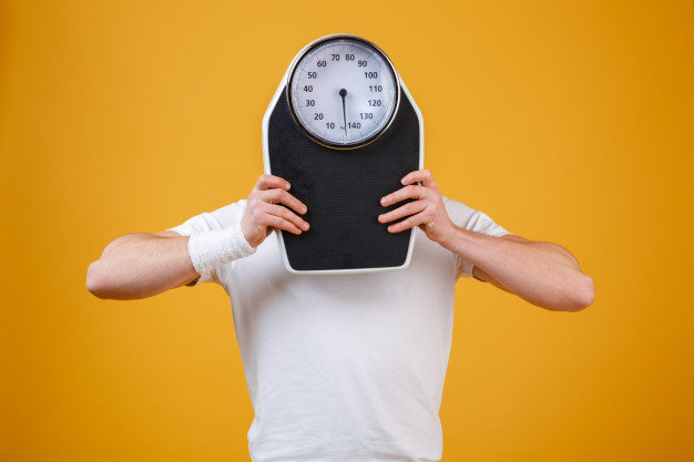 man hiding his face behind weight scale