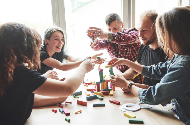group of creative friends sitting on a wooden table. people were having fun while playing a board game