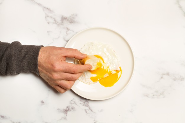 Man hand with a slice of bread and a broken fried egg on a white plate