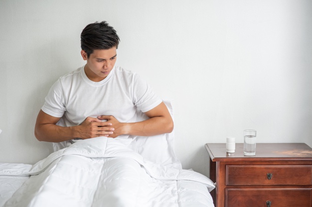man sits in bed with a stomachache and presses his stomach with his hands