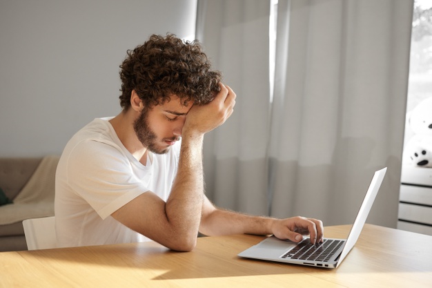 young male translator with thick beard and wavy hair touching head and closing eyes