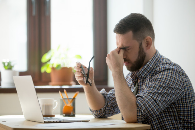 Stressed male massaging nose bridge suffering from headache 