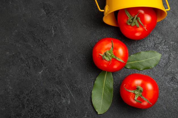 bucket with red tomatoes on dark table