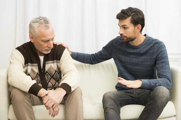 guy with hand on shoulder of aged sad man on sofa