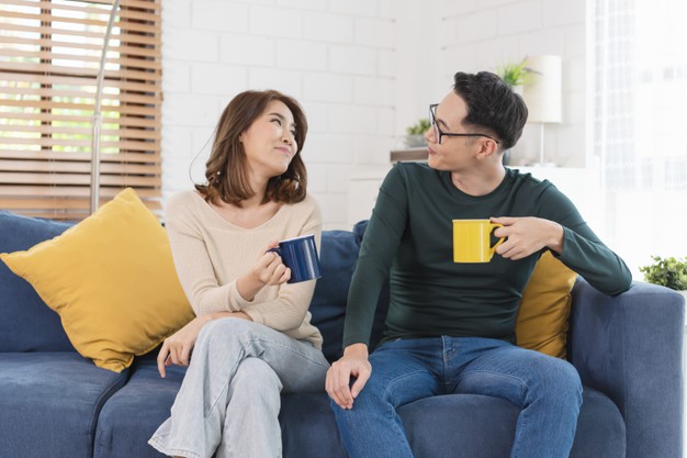 couple man and woman is spending weekend together on couch indoors at home, relaxing and enjoying drinking coffee