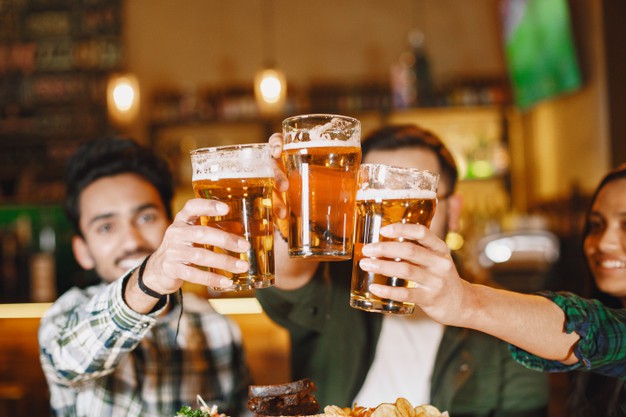 friends in a pub. guys and girl at bar. celebration over a mug of beer.