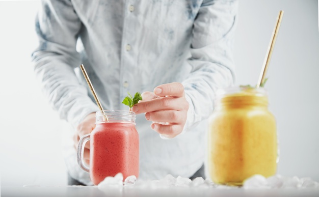 Man decorates smoothie in rustic jar with mint leaves. two jars with healthy different cold fruity smoothies
