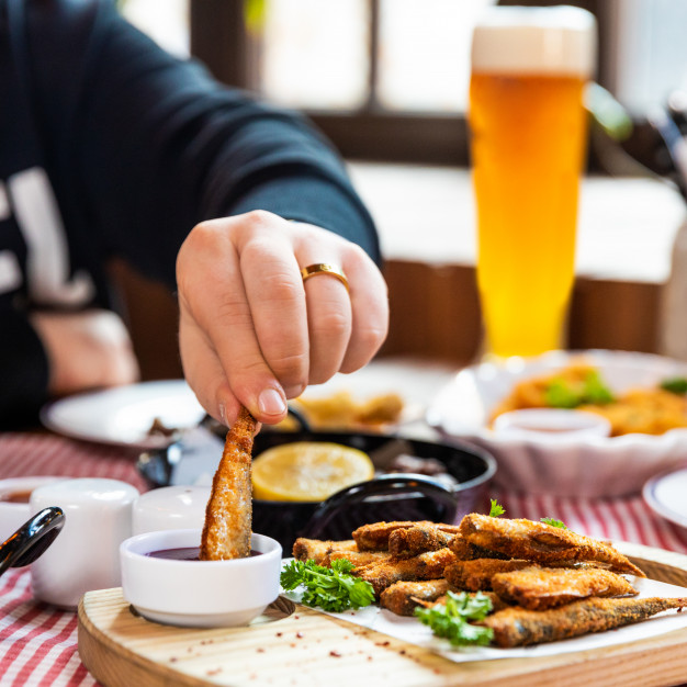 man-dipping-kilka-sprat-fish-ketchup-close-up