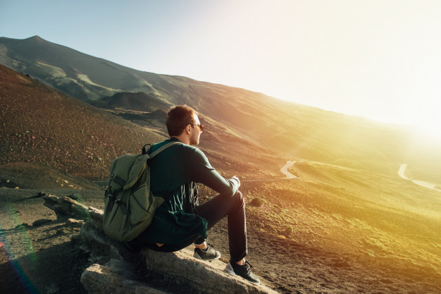 man-with-rucksack-sitting-rock-sunset-volcano-etna-mountain-sicily