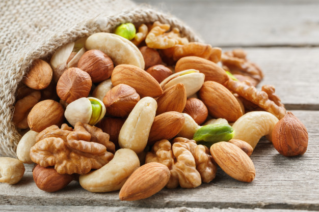 Mix of different nuts in a wooden cup against the background of fabric from burlap