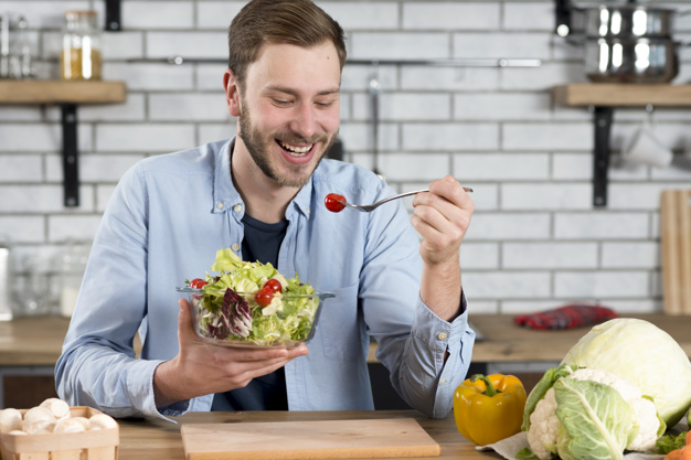 Portrait of a happy man eating fresh salad in the kitchen