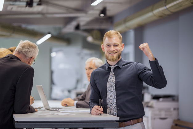 smiling businessman clenching his fist while team discussing in the background 