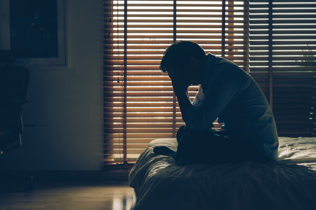 sad-businessman-sitting-head-hands-bed-dark-bedroom