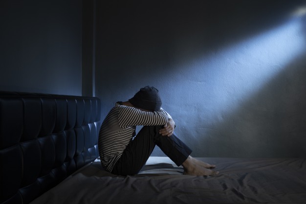 Sad man on the bed in the dark room