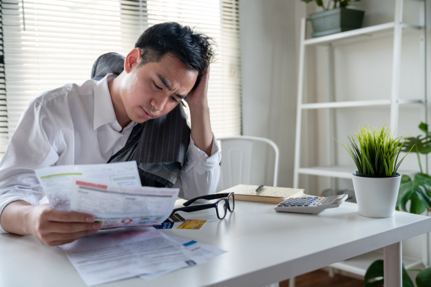 stressed-young-asian-businessman-holding-so-many-expenses-bills-such-as-electricity-bill-water-bill-internet-bill-cell-phone-bill-credit-card-bill-his-hand-no-money-pay-debt