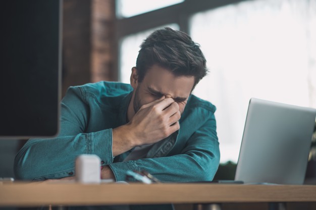 Unhappy cheerless man touching the bridge of the nose while feeling stressed