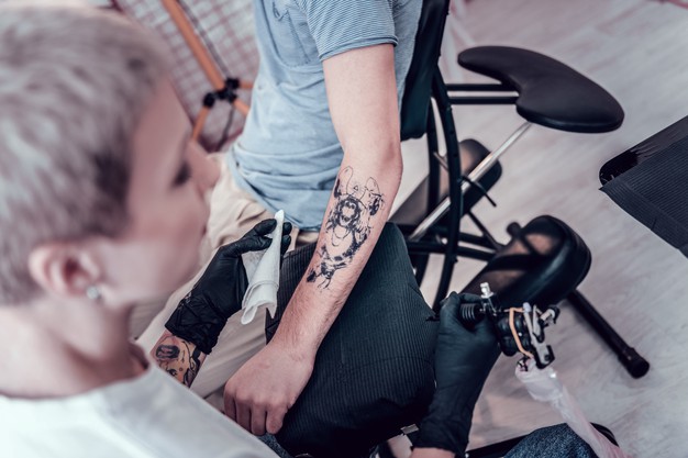Working with sketch. professional tattoo master carrying special machine and cloth and starting stuffing new tattoo