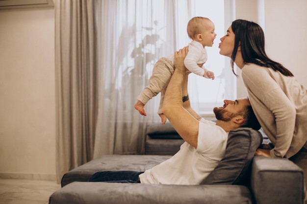Young family with toddler baby daughter sitting on coach at home