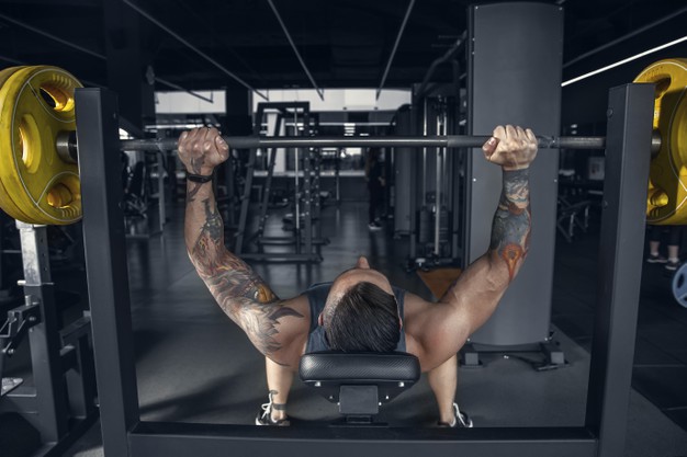  muscular caucasian athlete practicing pull-ups in gym with barbell