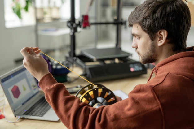 young-serious-designer-stretching-yellow-filament-from-spool-while-going-make-3d-print-new-object