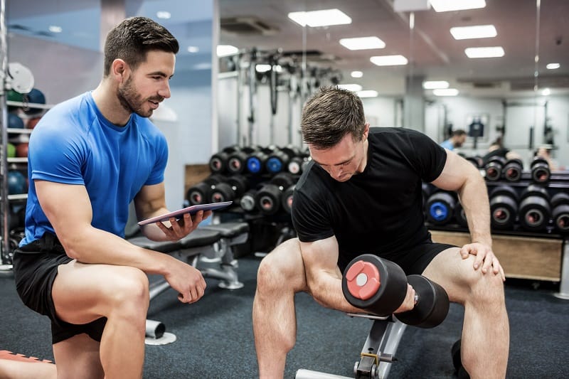 man doing workout at gym with his personal trainer