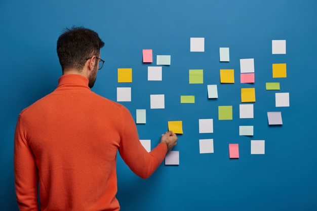 back-view-male-professional-works-puts-his-ideas-stick-notes-going-write-main-info-creating