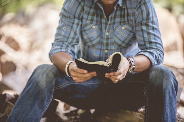 male in casual clothing reading the holy bible on a blurred 