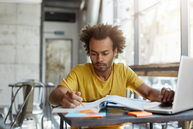 Focused young afro american english teacher checking his students' copybooks,