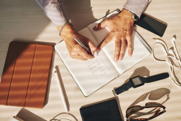 hands-man-writing-journal-gadgets-table