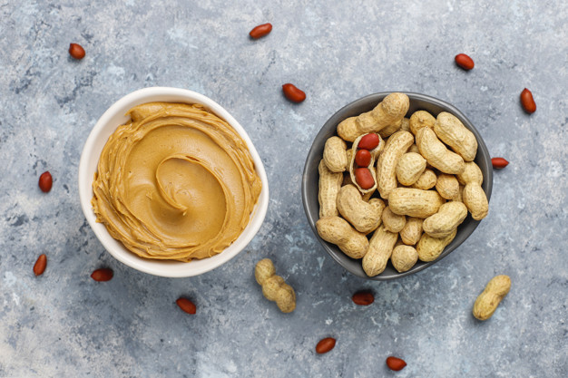 Homemade peanut butter with peanuts on grey concrete background