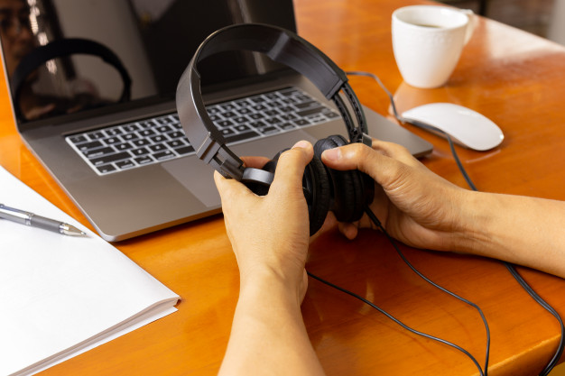 hands holding headphones and working on laptop computer at home