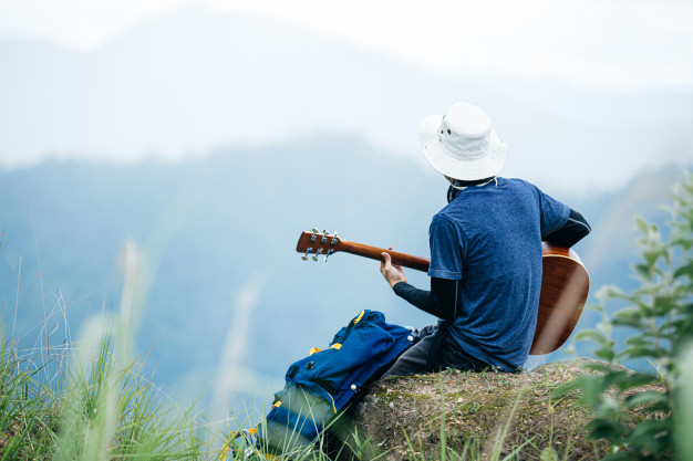 man sitting happily playing guitar in the forest alone