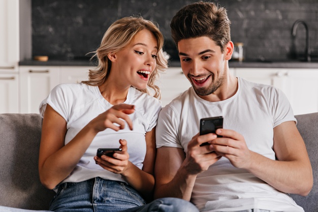 Smiling couple sitting on couch with phones. adorable young woman holding smartphone