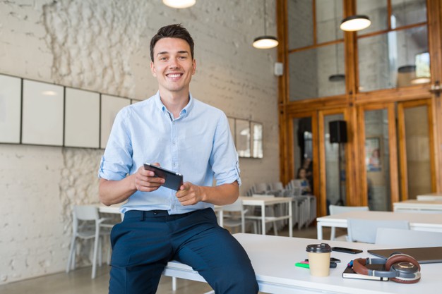 oung stylish smiling man in co-working office, startup freelancer holding using tablet