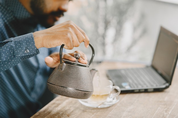 an with beard sitting in a cafe and pouring a tea