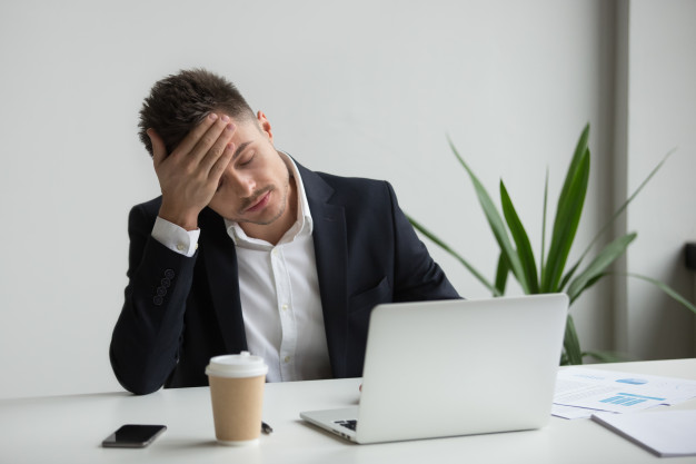Frustrated millennial businessman having strong headache tired from laptop work 