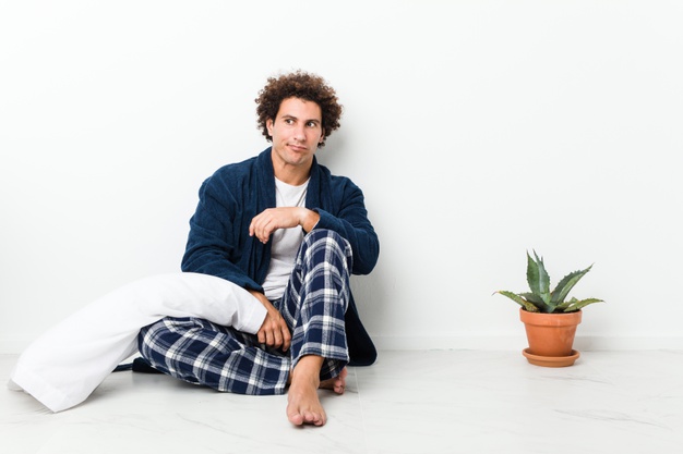 man wearing pajama sitting on house floor confused