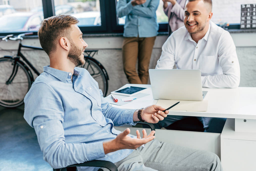 young men multicultural programmers gesturing during discussion in office