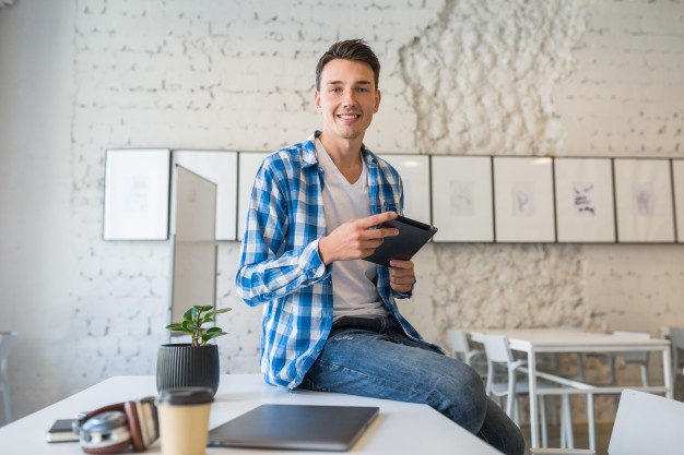 Looking young handsome man sitting in co-working office 