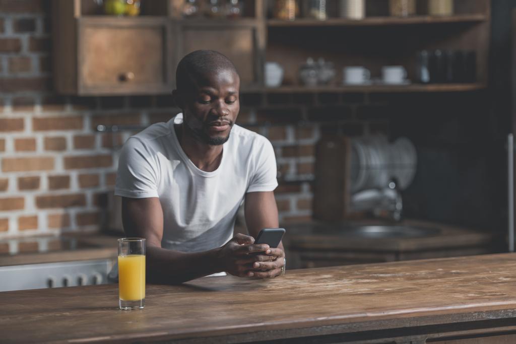 African american man using phone while sitting in kitchen