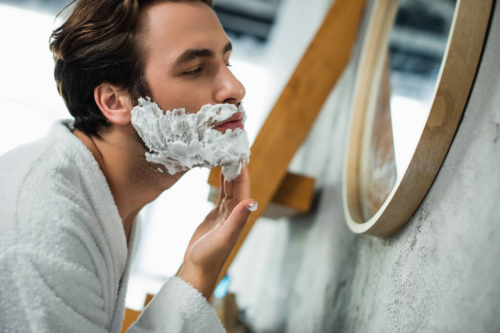 Man applying shaving cream on face near mirror