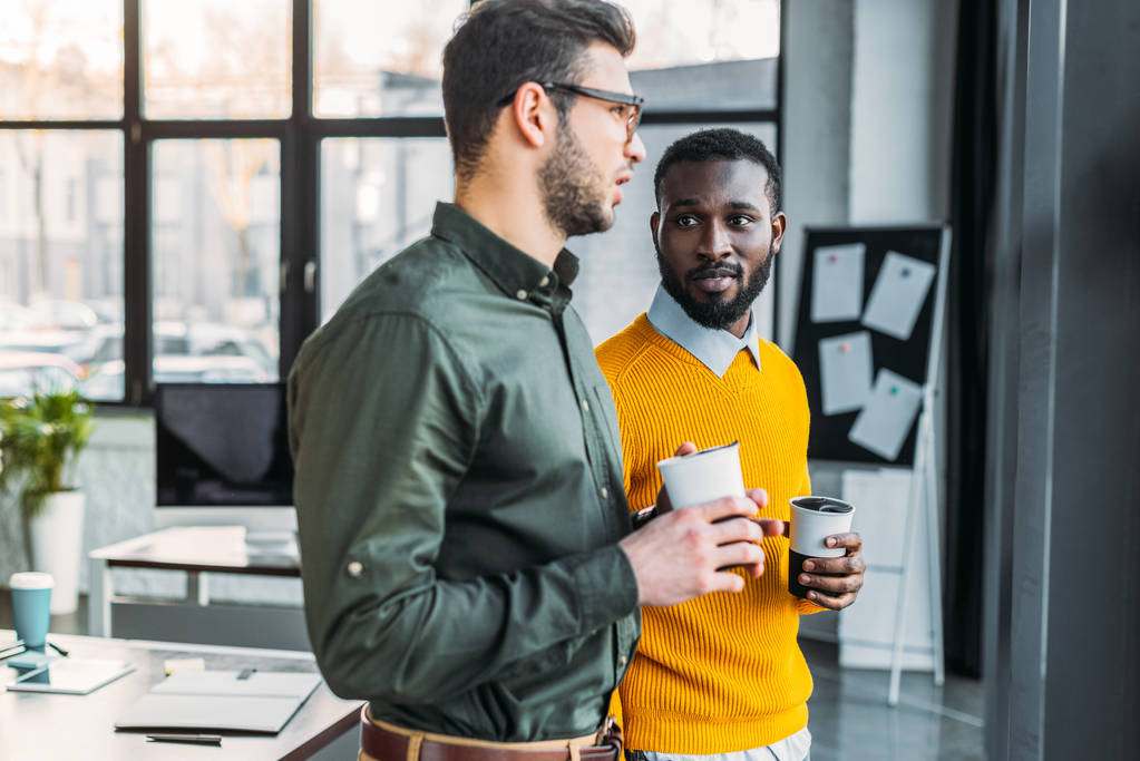 men talking and holding cups of coffee