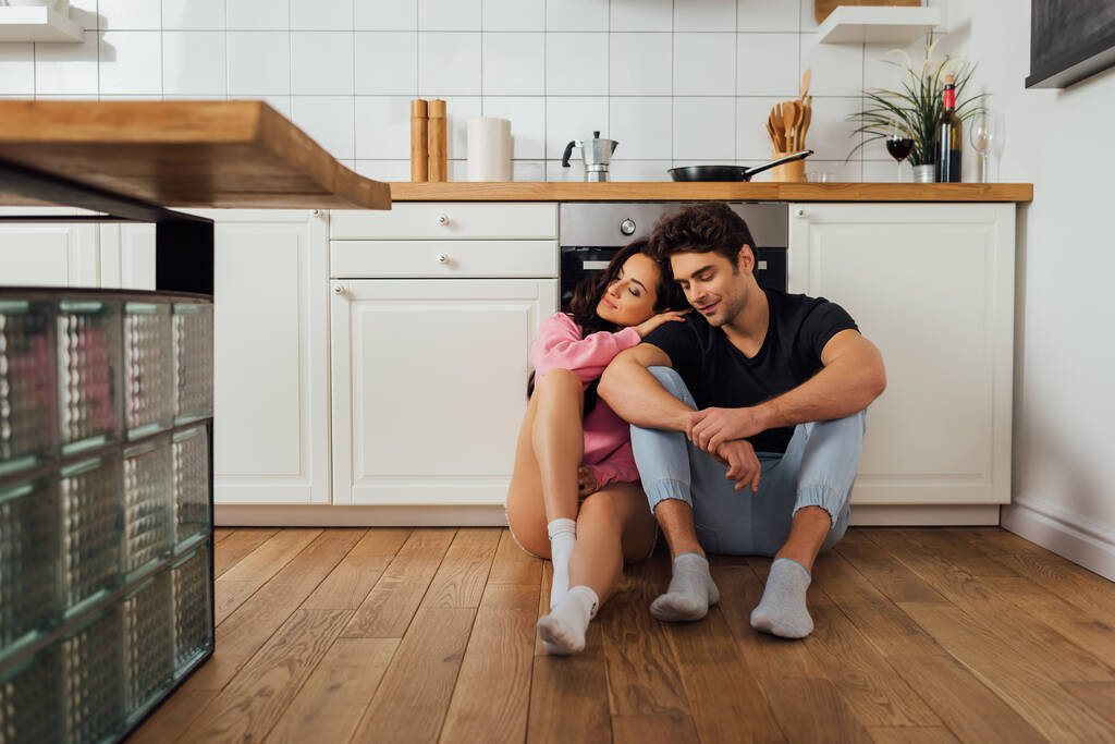 beautiful woman hugging boyfriend with closed eyes on kitchen floor